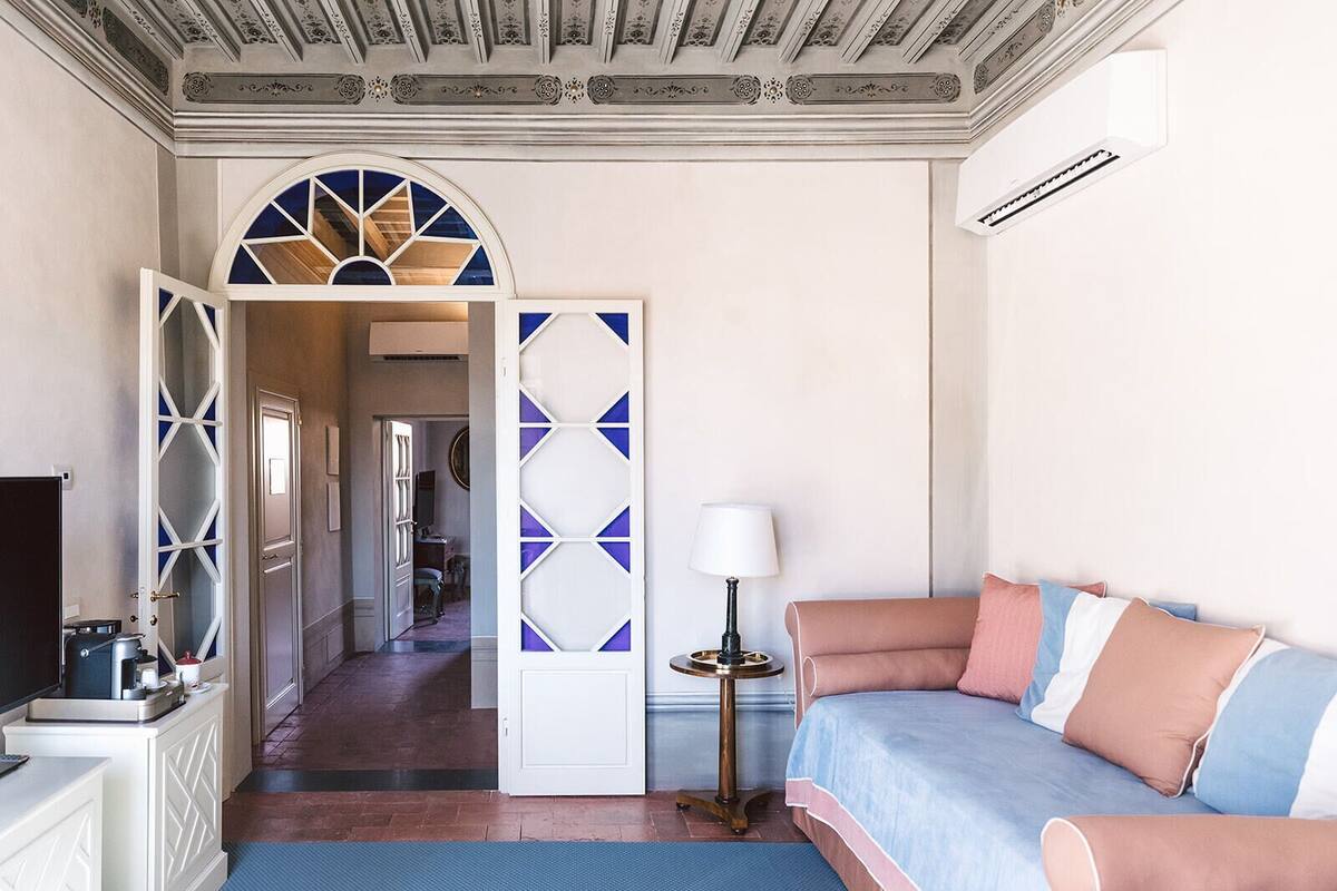 A hotel room with a bed, a desk, a lamp, and a view of the hallway.