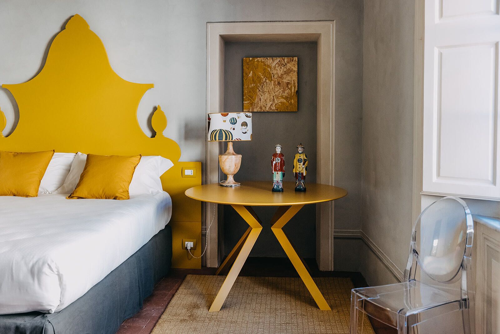 Una habitación de hotel con una cama, una mesita de noche con lámpara y un espejo.