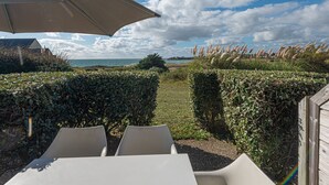 A patio with a table and chairs, a large umbrella, and a view of the sea and sky.