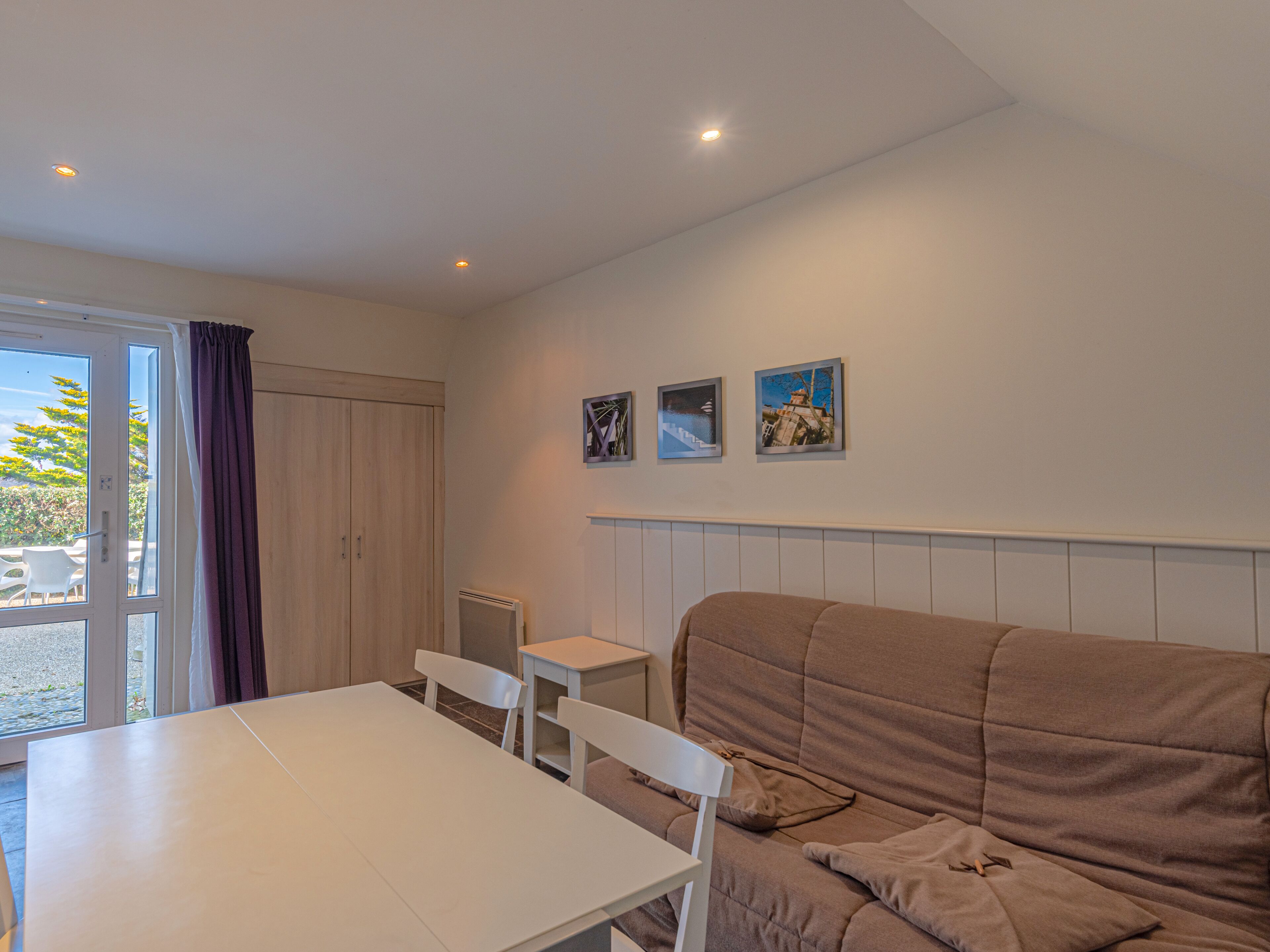 Ein Zimmer mit einem weißen Tisch, zwei weißen Stühlen, einem braunen Sofa und einem Fenster mit Vorhängen.