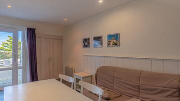 Ein Zimmer mit einem weißen Tisch, zwei weißen Stühlen, einem braunen Sofa und einem Fenster mit Vorhängen.