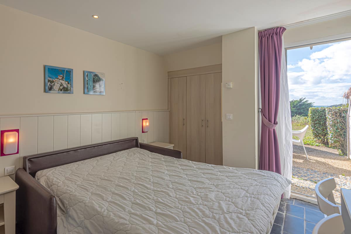 Un dormitorio con cama, mesita de noche, armario y ventana con cortinas.