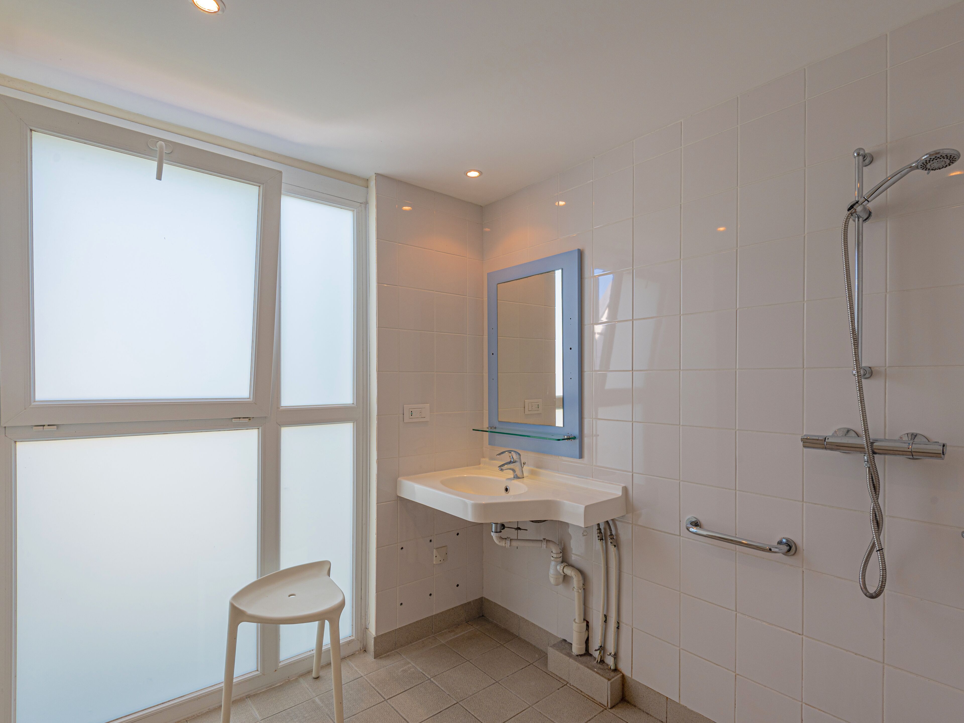 A bathroom with a window, a sink, a mirror, and a shower.