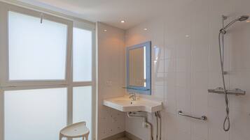 Een badkamer met een raam, een wastafel, een spiegel en een douche.