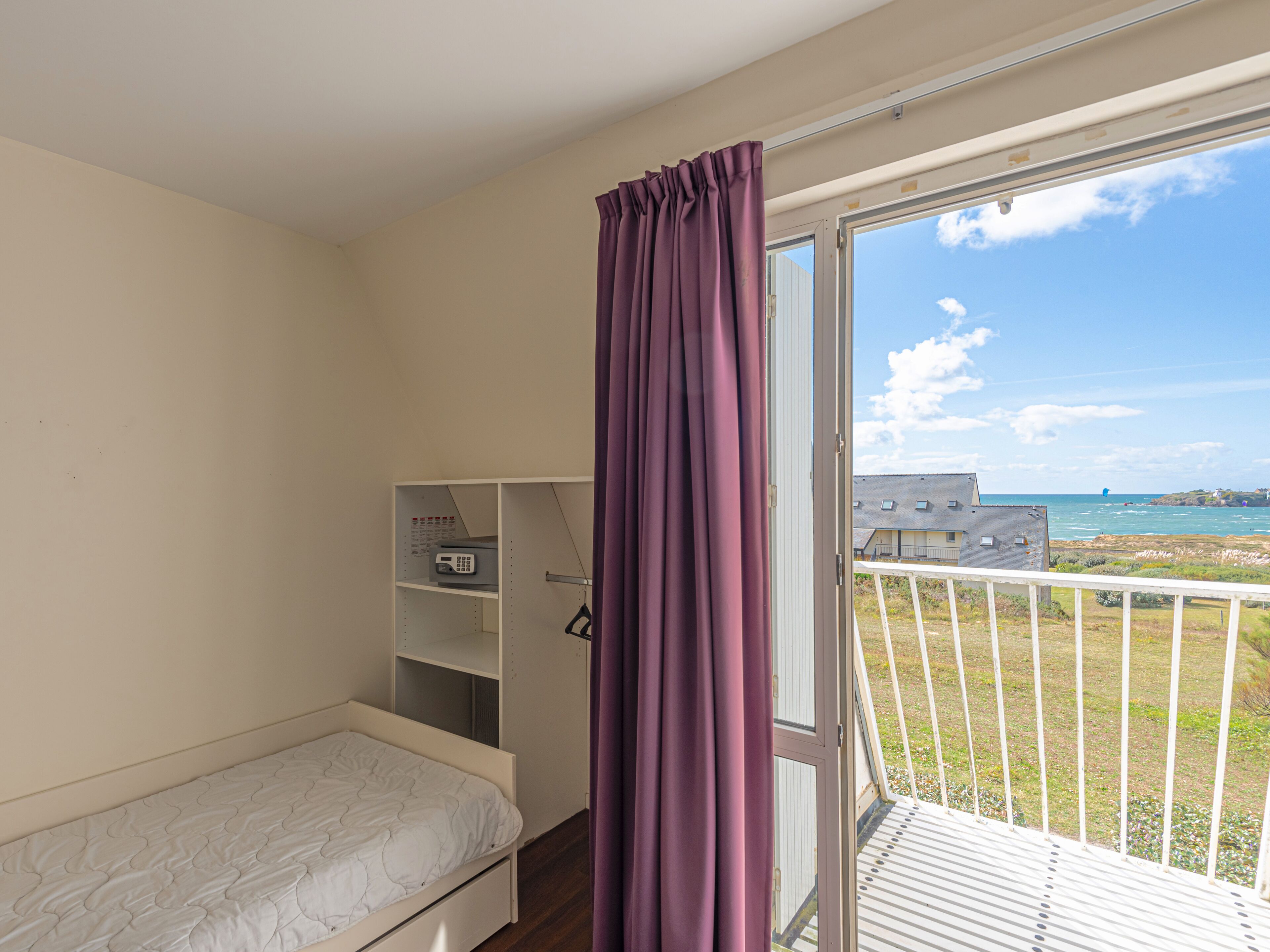 A bedroom with a single bed, a wardrobe, and a balcony with a view of the sea.