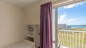 A bedroom with a single bed, a wardrobe, and a balcony with a view of the sea.