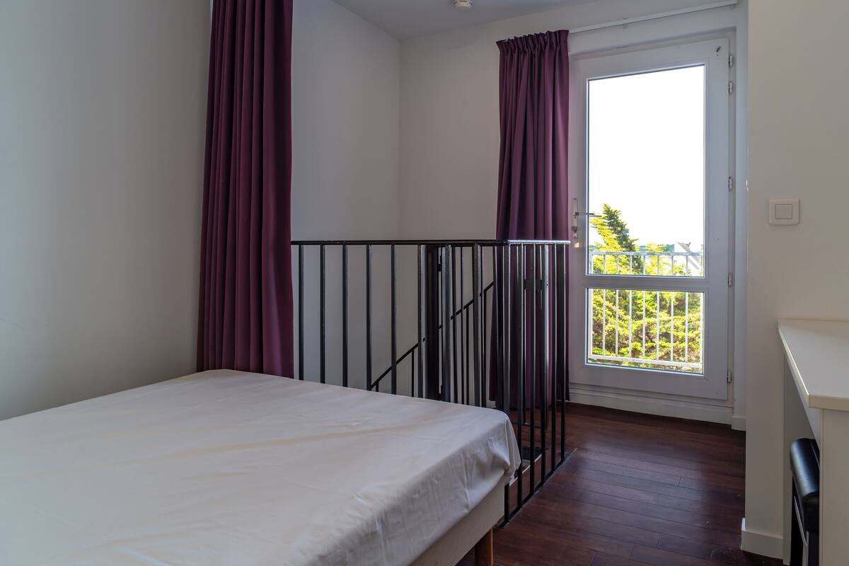 Un dormitorio con cama, ventana con cortinas, balcón y puerta.