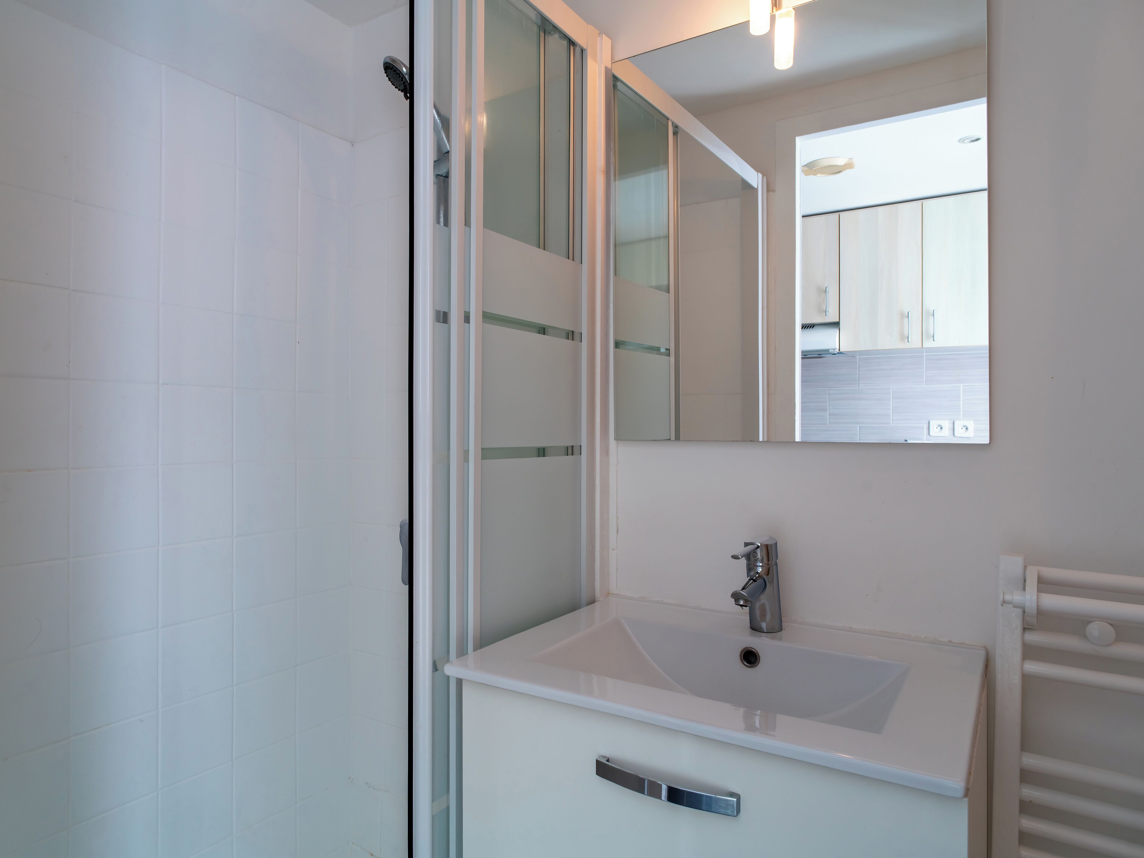 Een moderne badkamer met een douchecabine van glas, een witte wastafel met één kraan, en een spiegel boven de wastafel.
