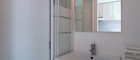Een moderne badkamer met een douchecabine van glas, een witte wastafel met één kraan, en een spiegel boven de wastafel.