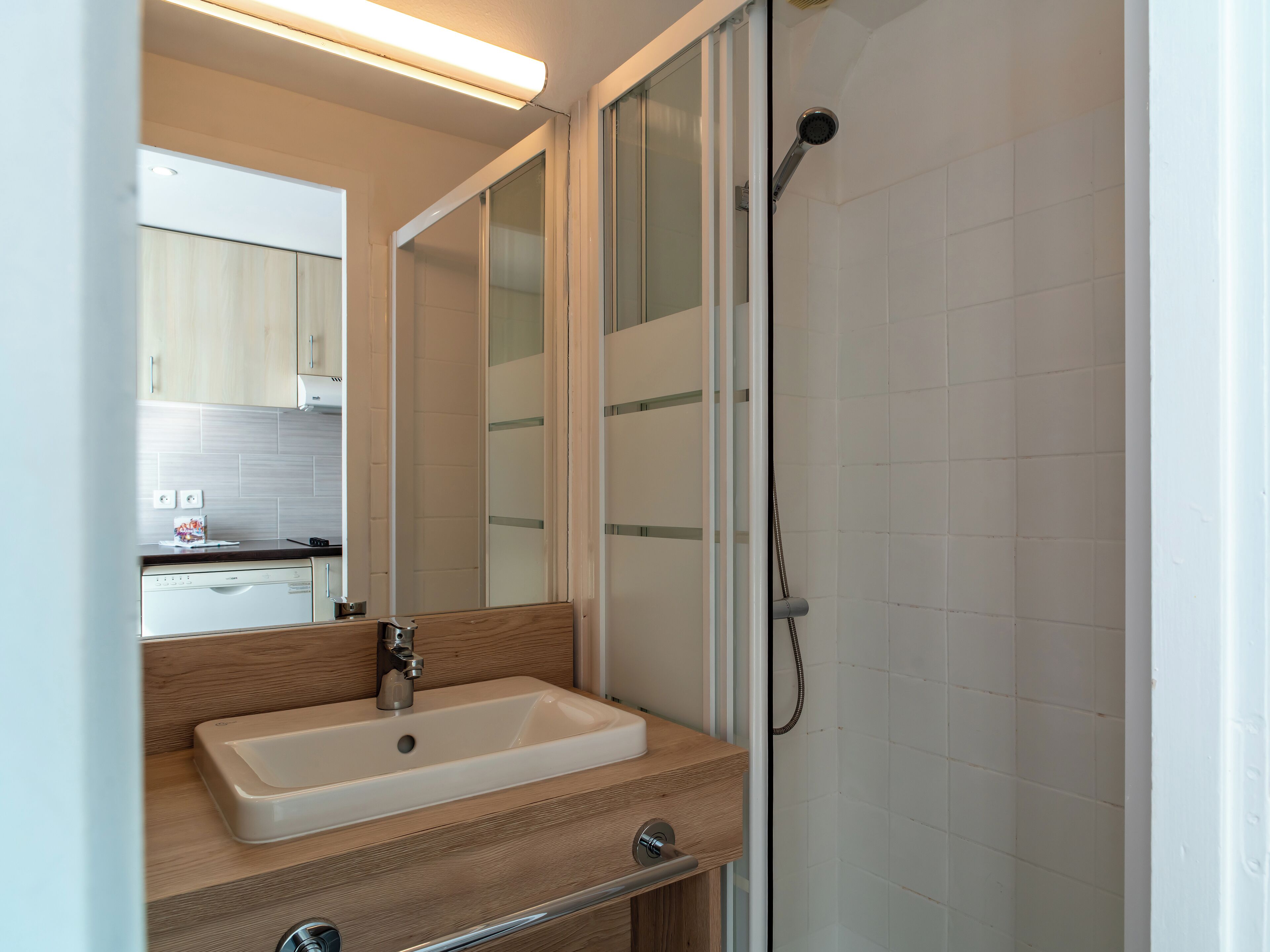 A modern bathroom with a wooden vanity, a white sink, and a glass shower enclosure.