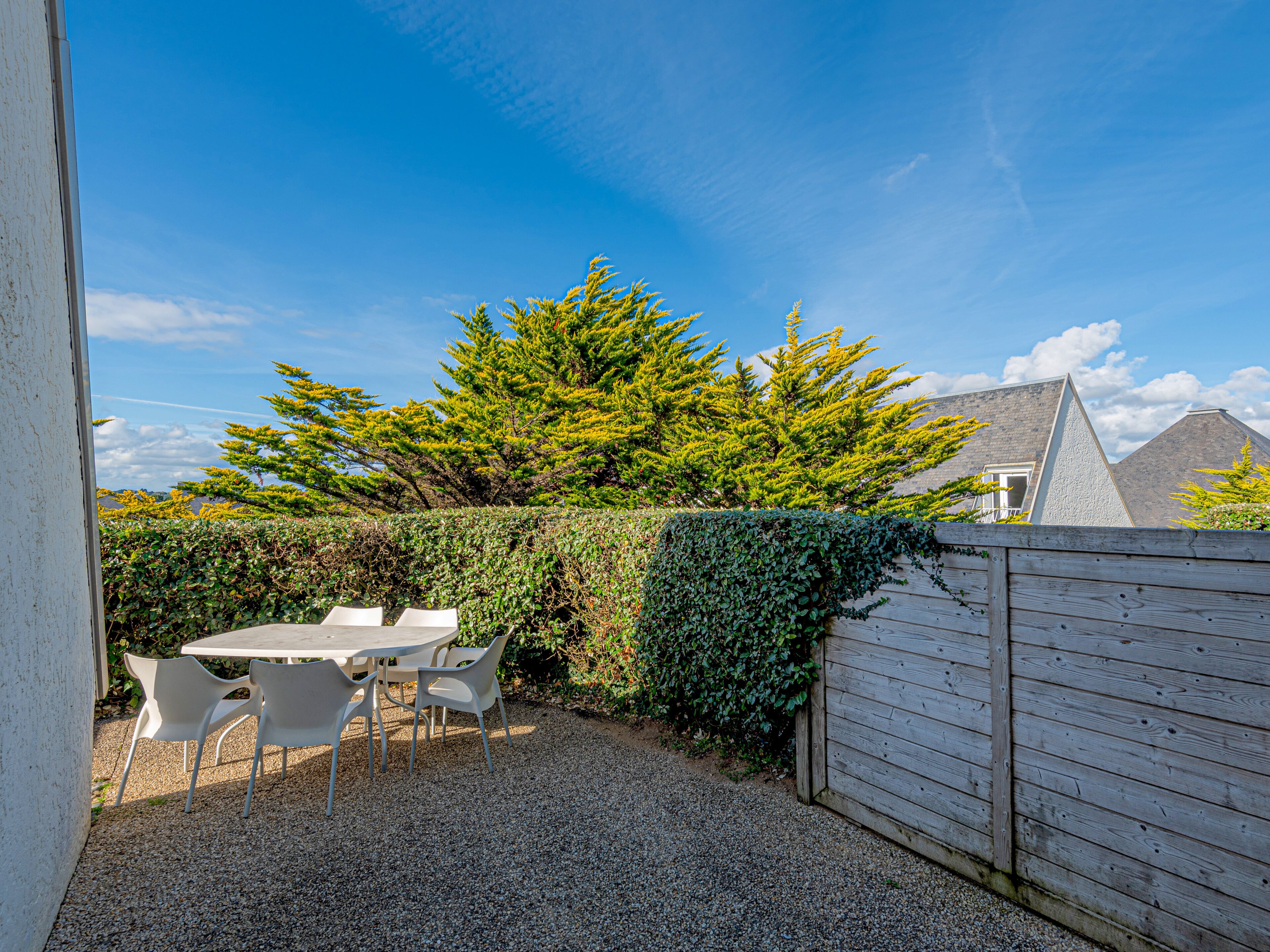 A patio with a table and chairs, surrounded by a wooden fence and a hedge.
