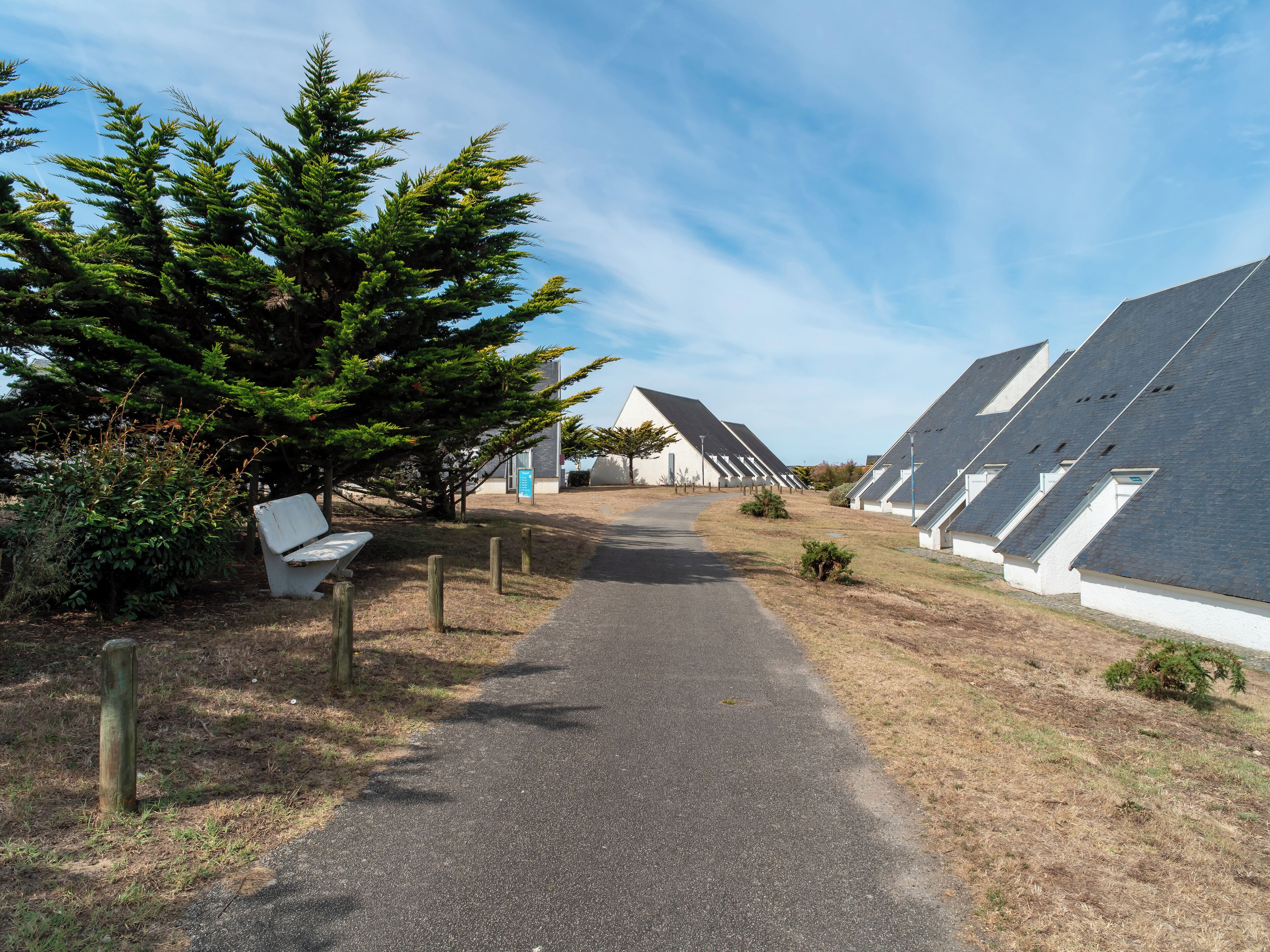 Un chemin mène à une rangée de bâtiments modernes, coiffés de toits blancs, sous un ciel dégagé.
