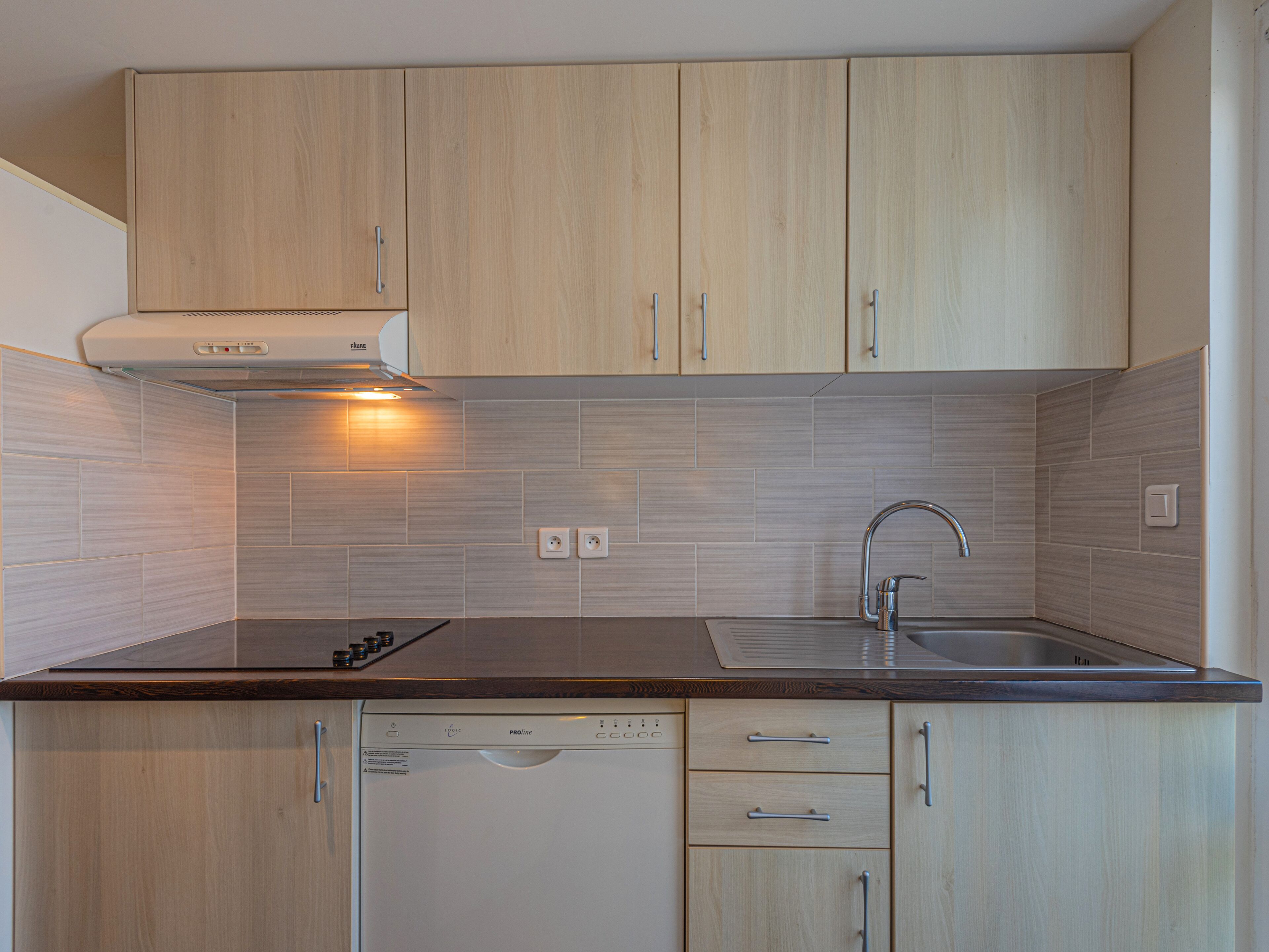 A modern kitchen with light wood cabinets, a stainless steel sink, and a dishwasher.
