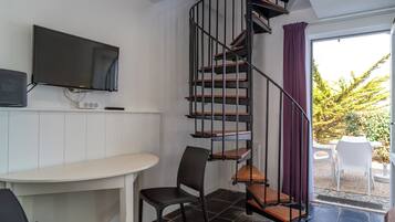A modern room with a spiral staircase, a flat-screen TV, a dining area, and a view of the outdoors.