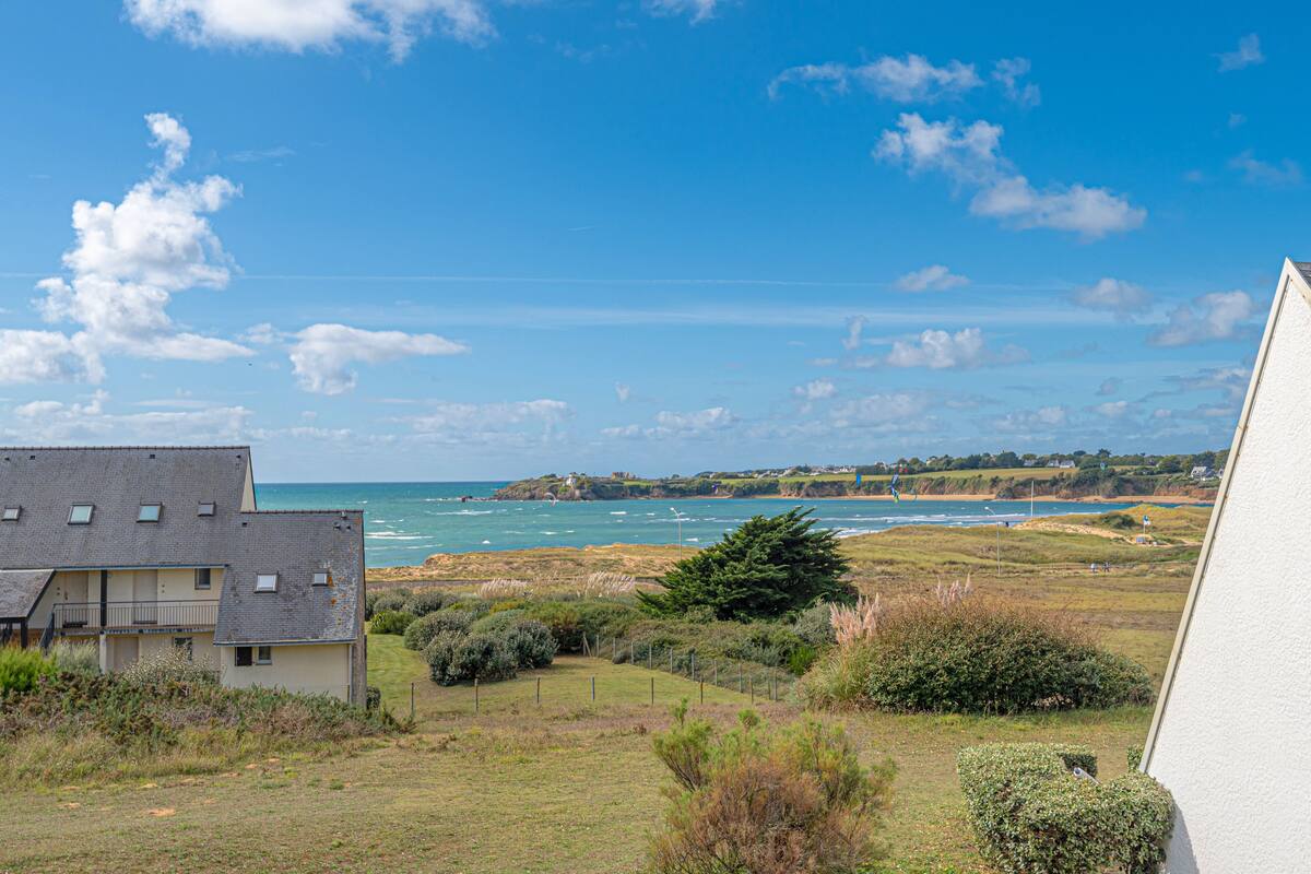 Vista costera con un edificio en primer plano y una playa al fondo.