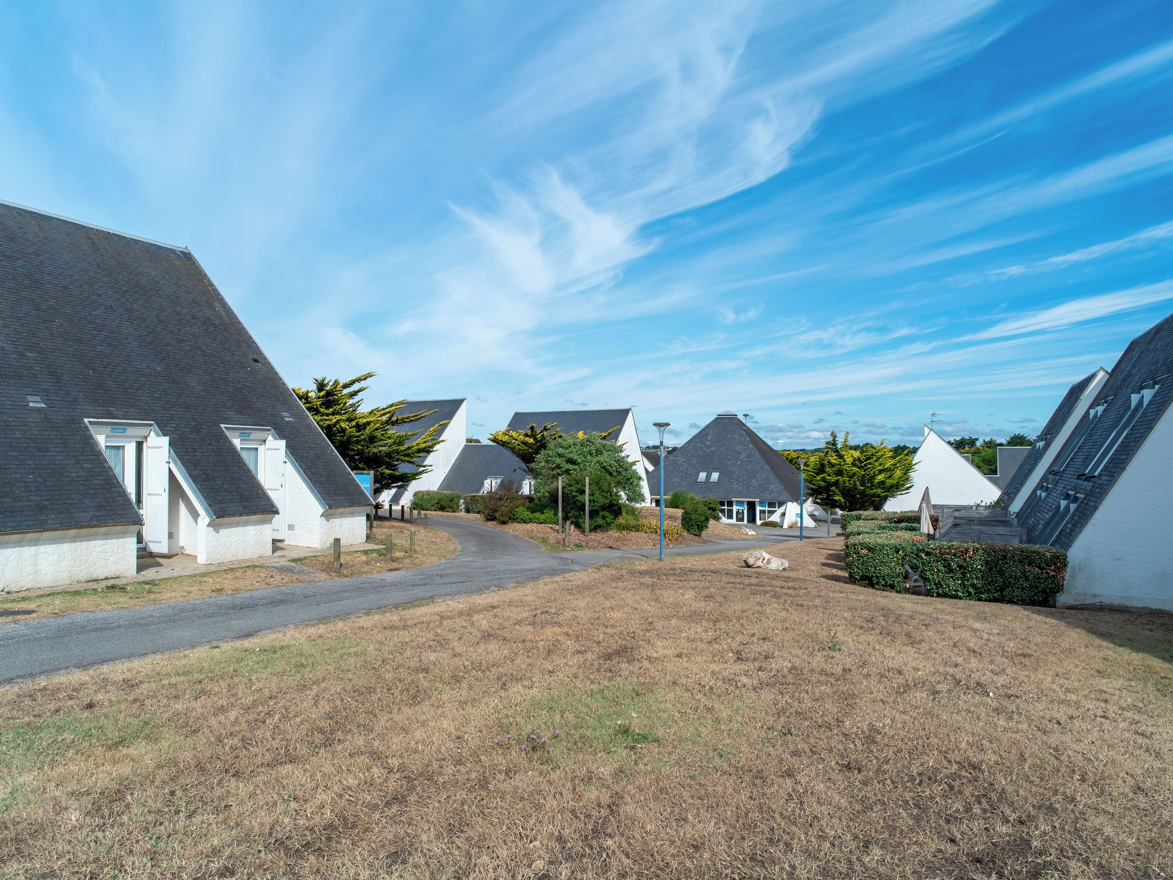 A row of modern, white houses with steep roofs, a clear sky, and a dry grassy area in front.