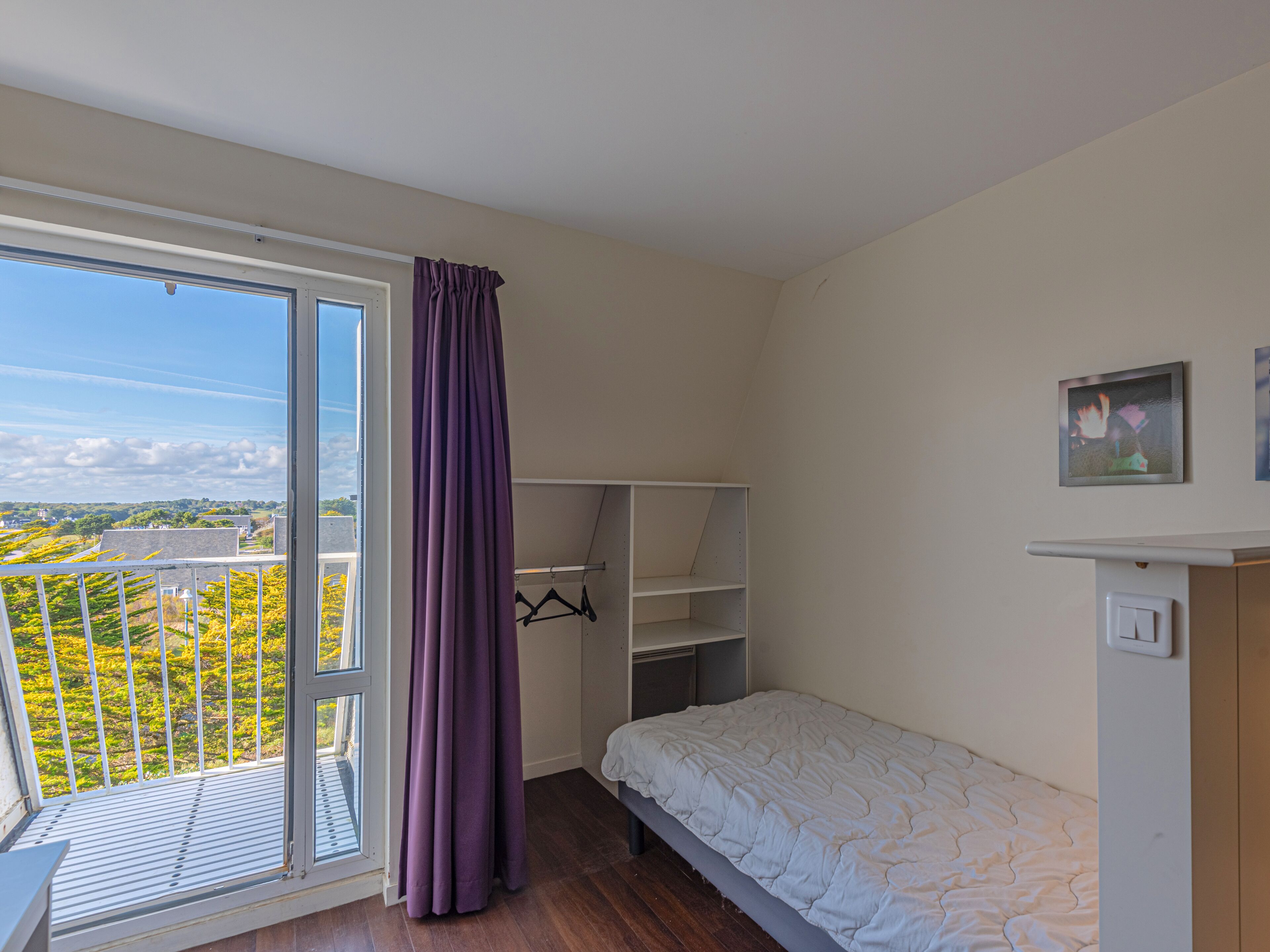 Un dormitorio con cama, armario, ventana con cortina y vistas a zonas verdes.