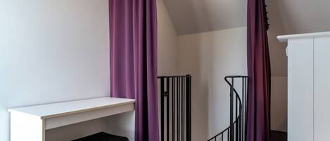 A room with a white desk, a black stool, purple curtains, and a white wardrobe.