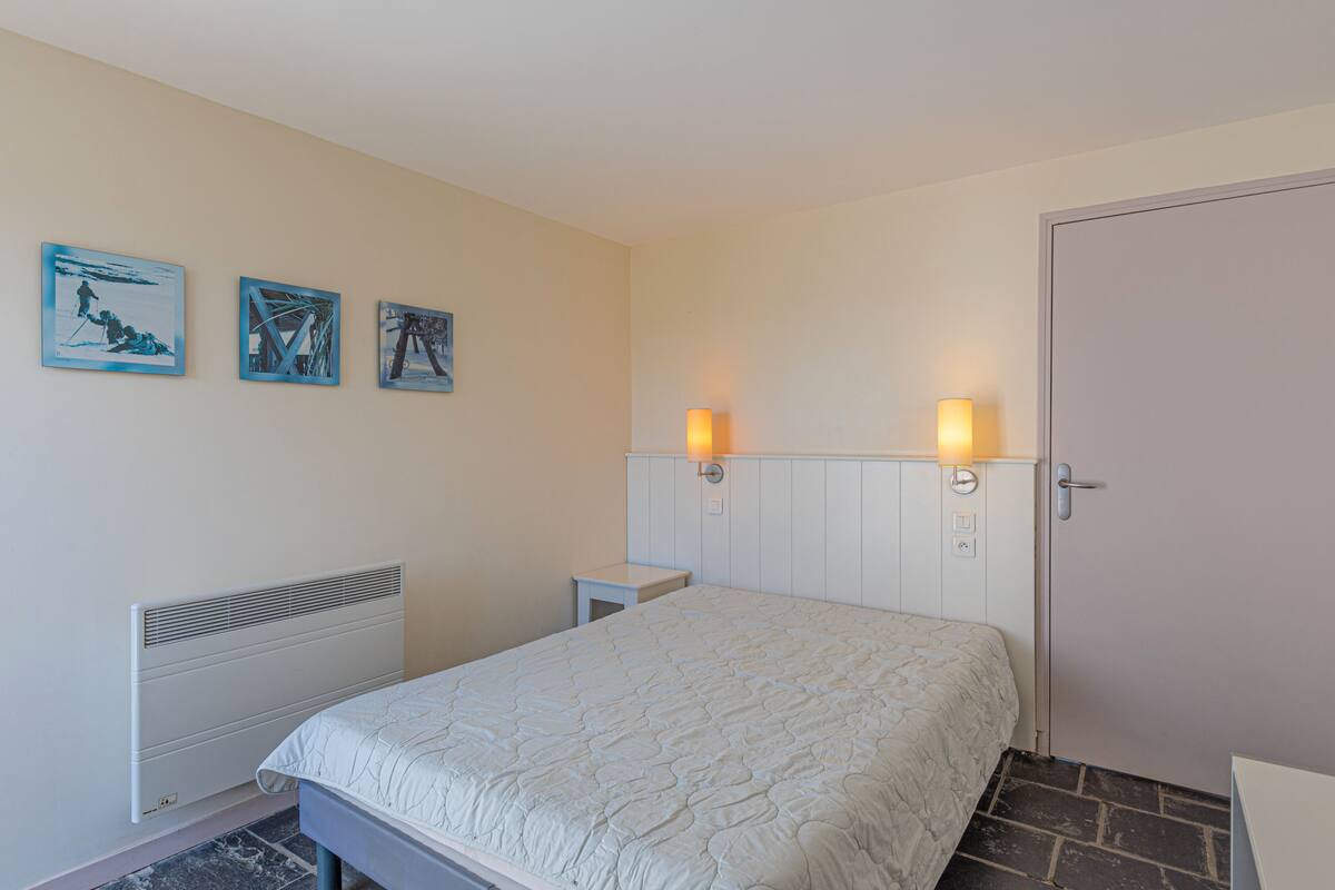 Un dormitorio con una cama, un radiador, una puerta y tres cuadros en la pared.
