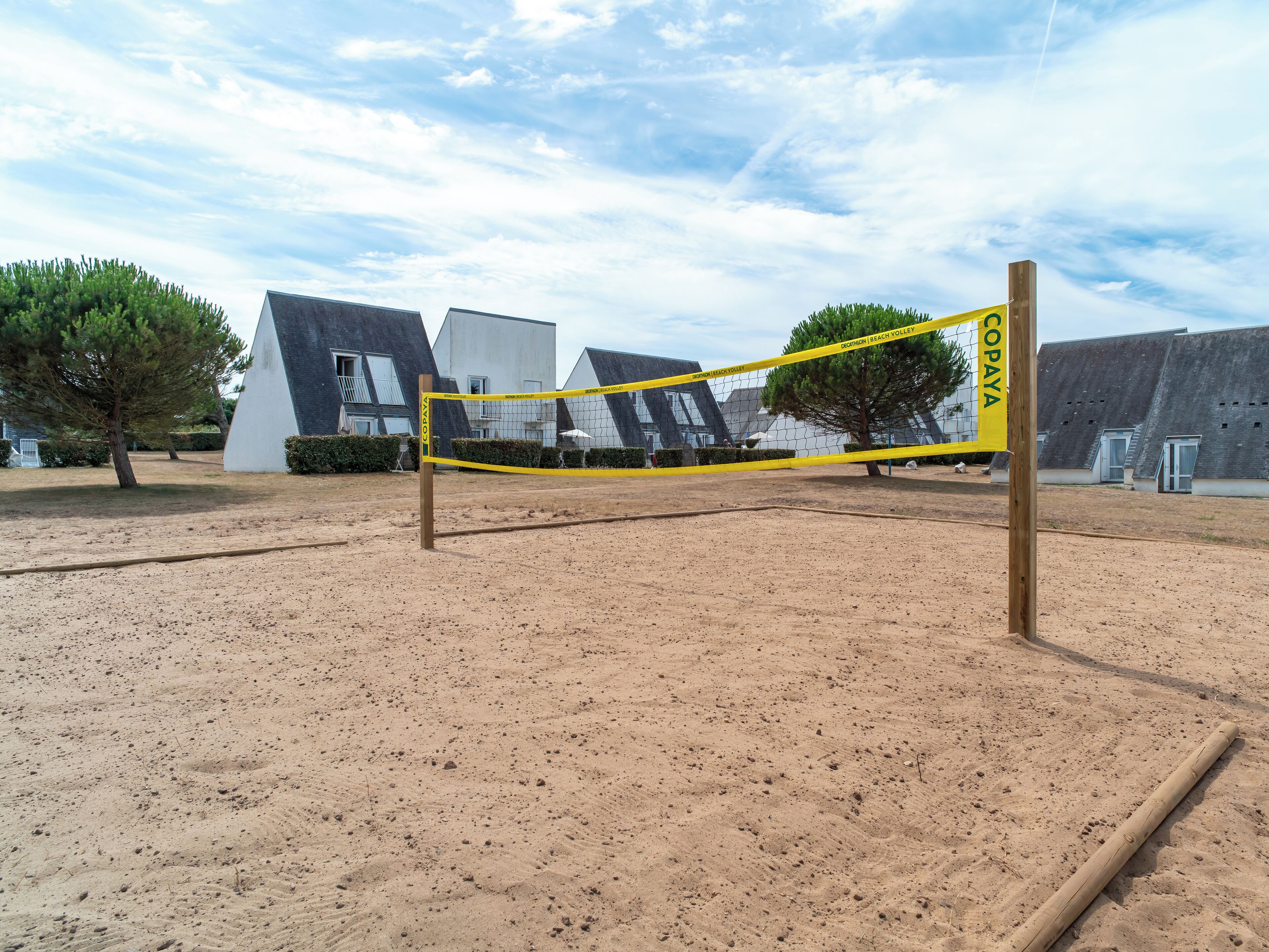 A volleyball court with a net, surrounded by sandy ground and trees.