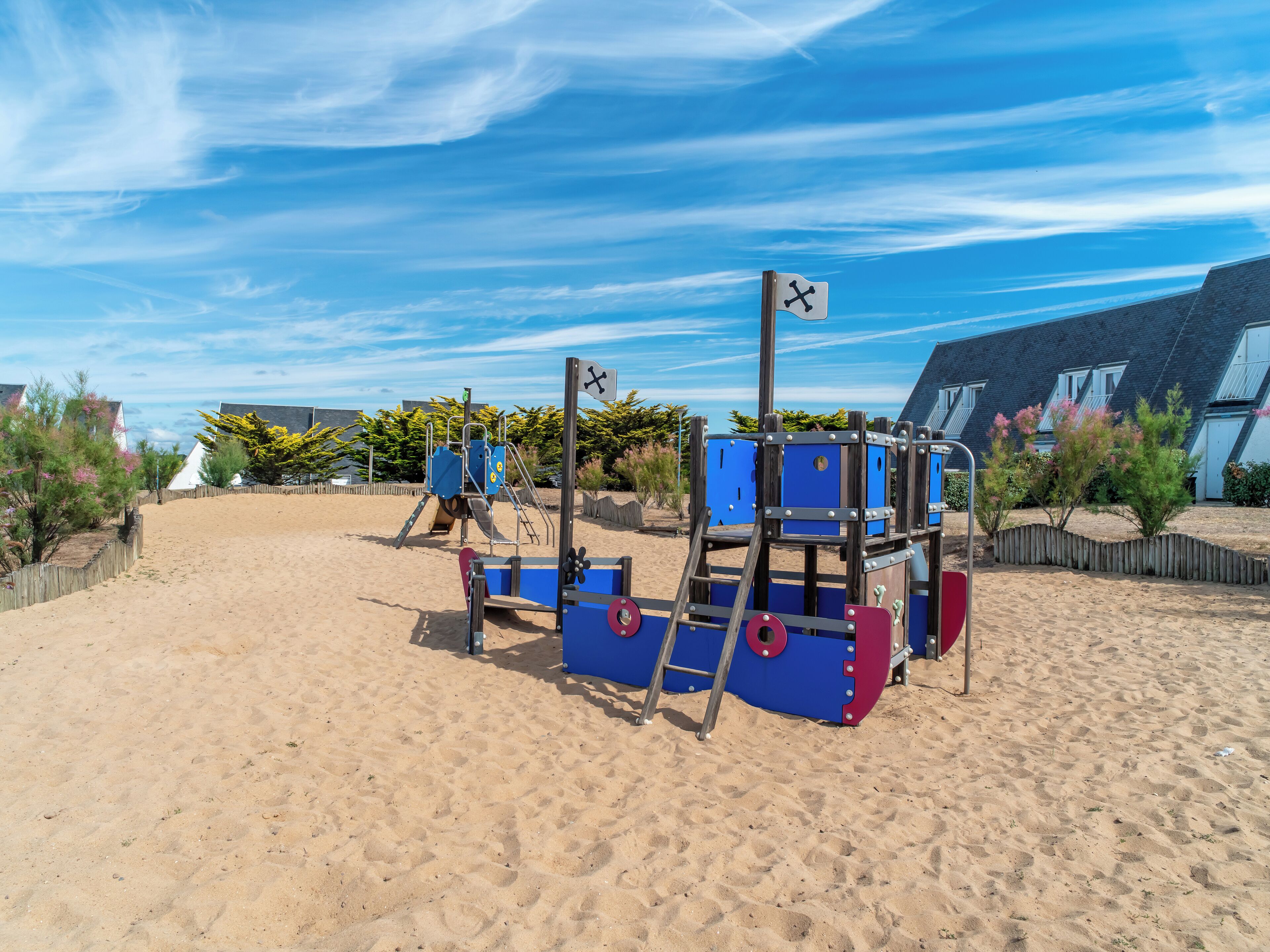 A sandy beach with a playground structure featuring a slide and climbing elements.
