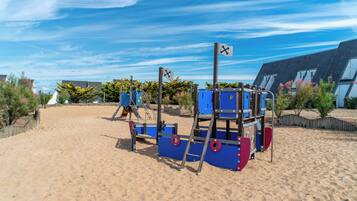 A sandy beach with a playground structure featuring a slide and climbing elements.