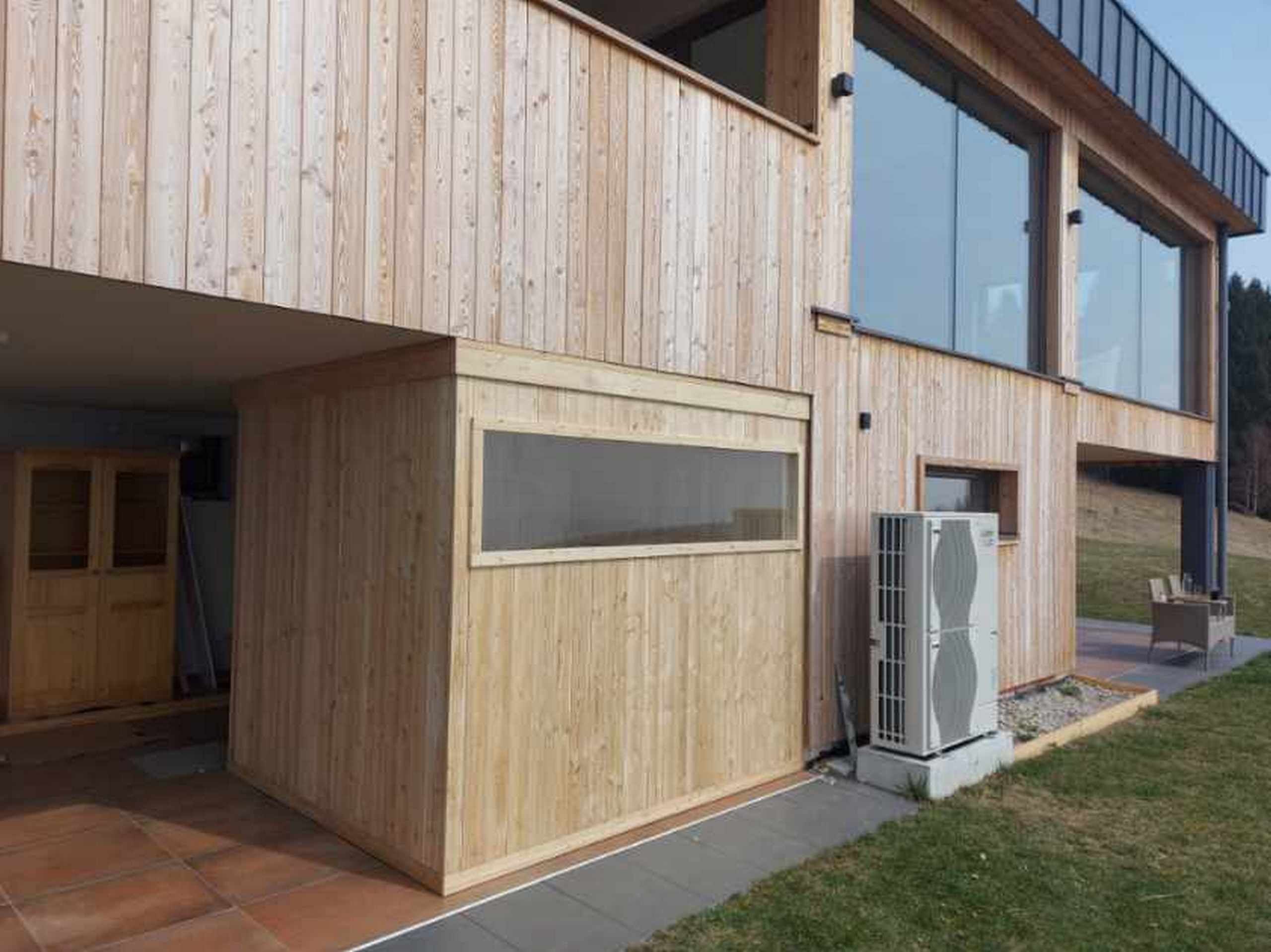 A modern wooden building with large windows and a visible air conditioning unit.