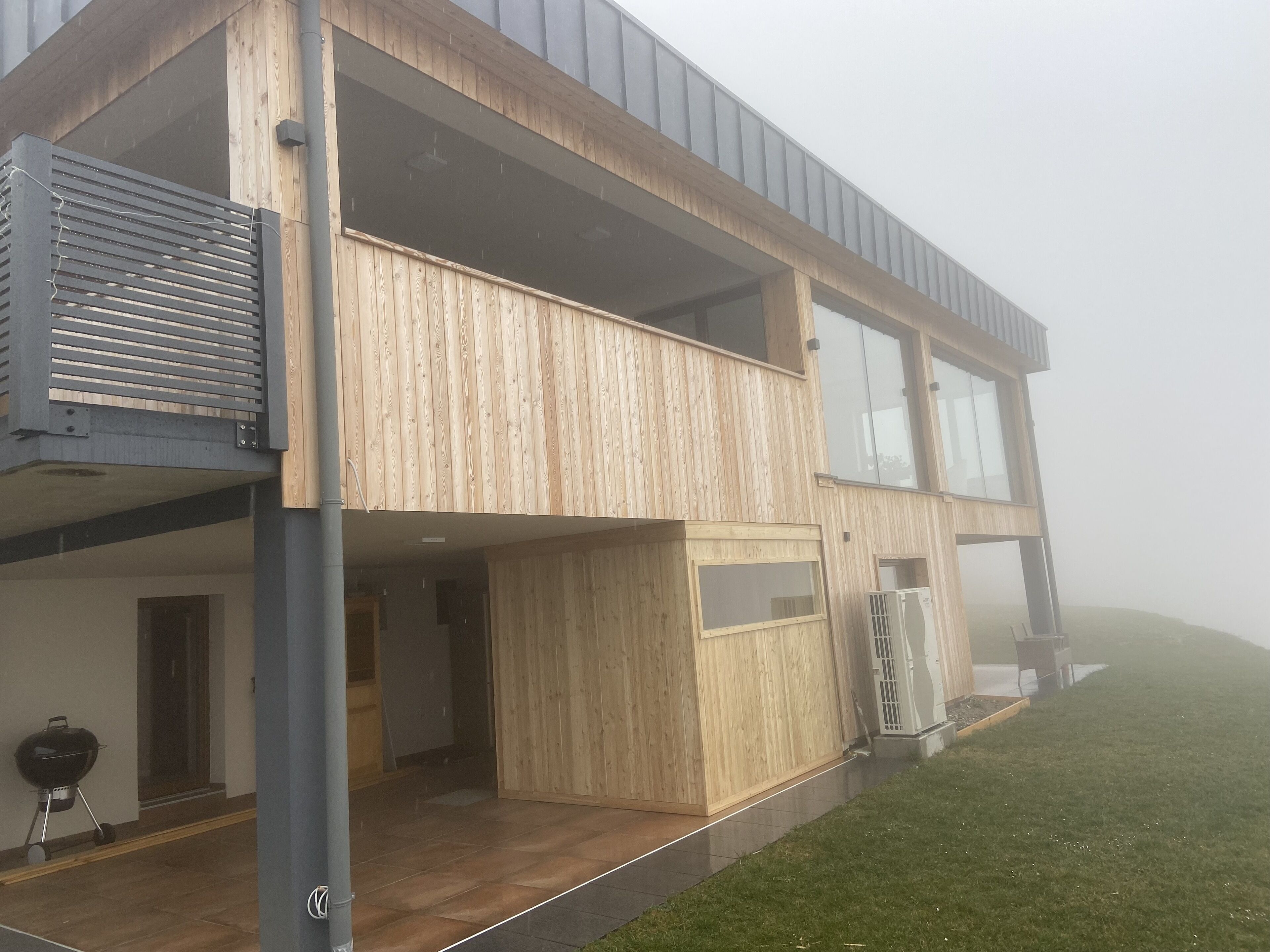 Ein modernes, zweistöckiges Haus mit Holzfassade, großen Fenstern und einem Balkon.