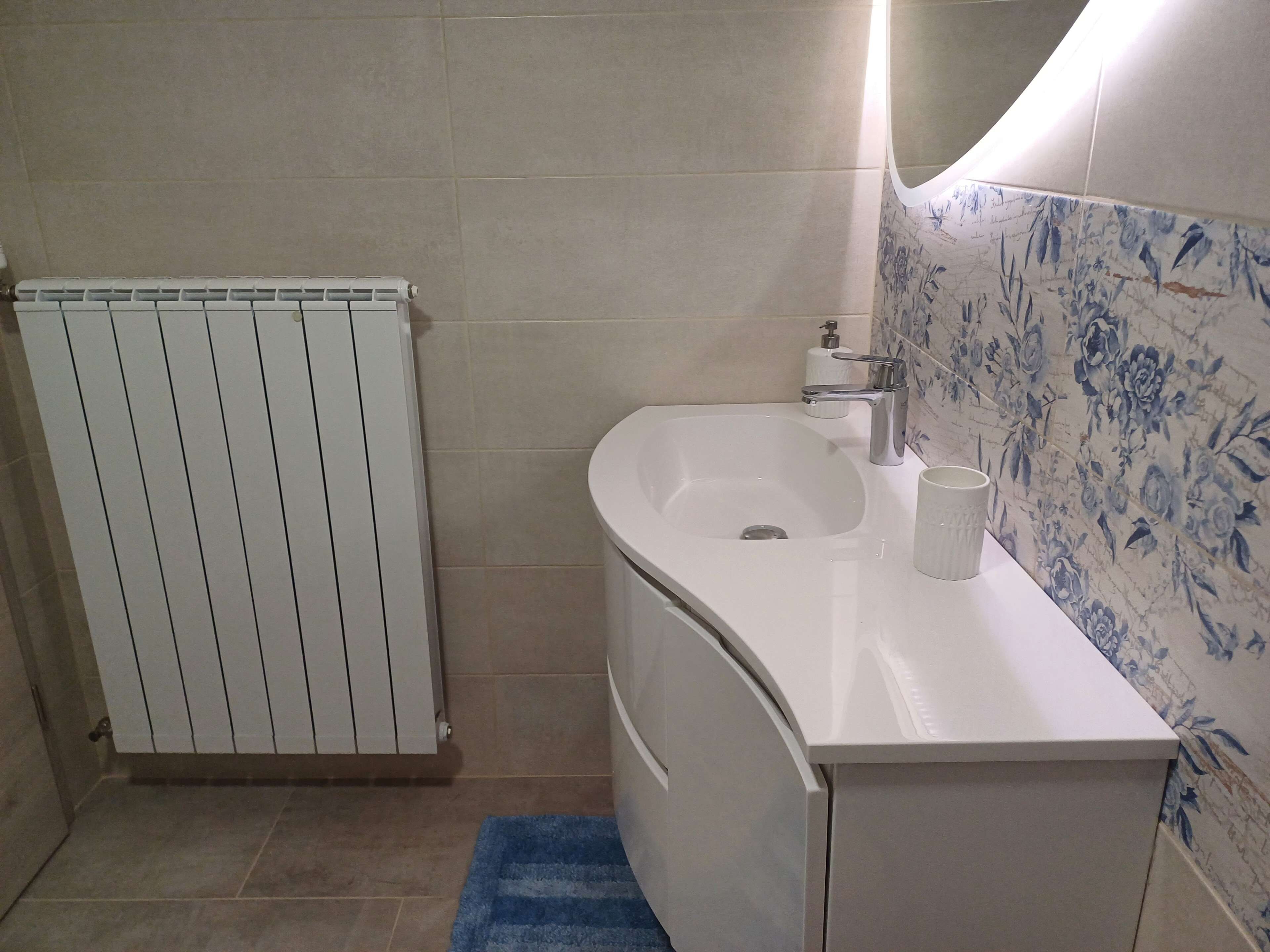 A bathroom with a white sink, a mirror, and a blue towel on the floor.