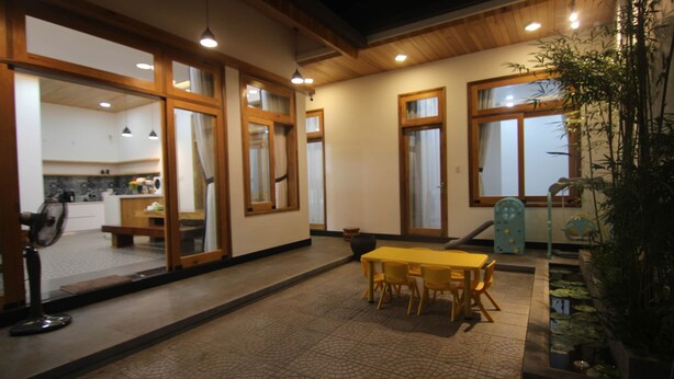 Un espace intérieur spacieux comprenant une table et des chaises, des fenêtres à cadre en bois et un petit jardin intérieur.