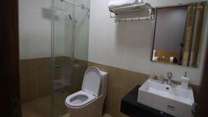Une salle de bain avec une douche à parois de verre, des toilettes blanches, un lavabo avec un miroir au-dessus et un porte-serviettes avec des serviettes.
