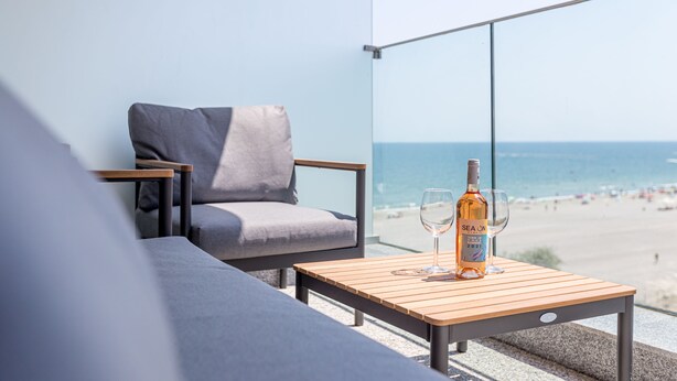 A balcony with a wooden table, a grey sofa, and a bottle of wine. - Sea On (Navodari)