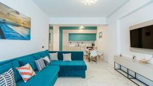 A modern living room with a teal sofa, a dining area, and a kitchen with teal cabinets. - Sea On (Navodari)