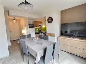 Una cocina moderna con microondas, horno y lavabo. Hay una zona de comedor con mesa y sillas, y un televisor sobre un mueble.