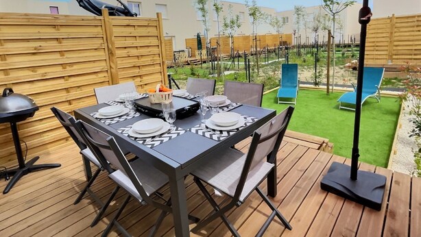 Un patio con una mesa lista para comer, rodeado de piso de madera y un paraguas rojo.