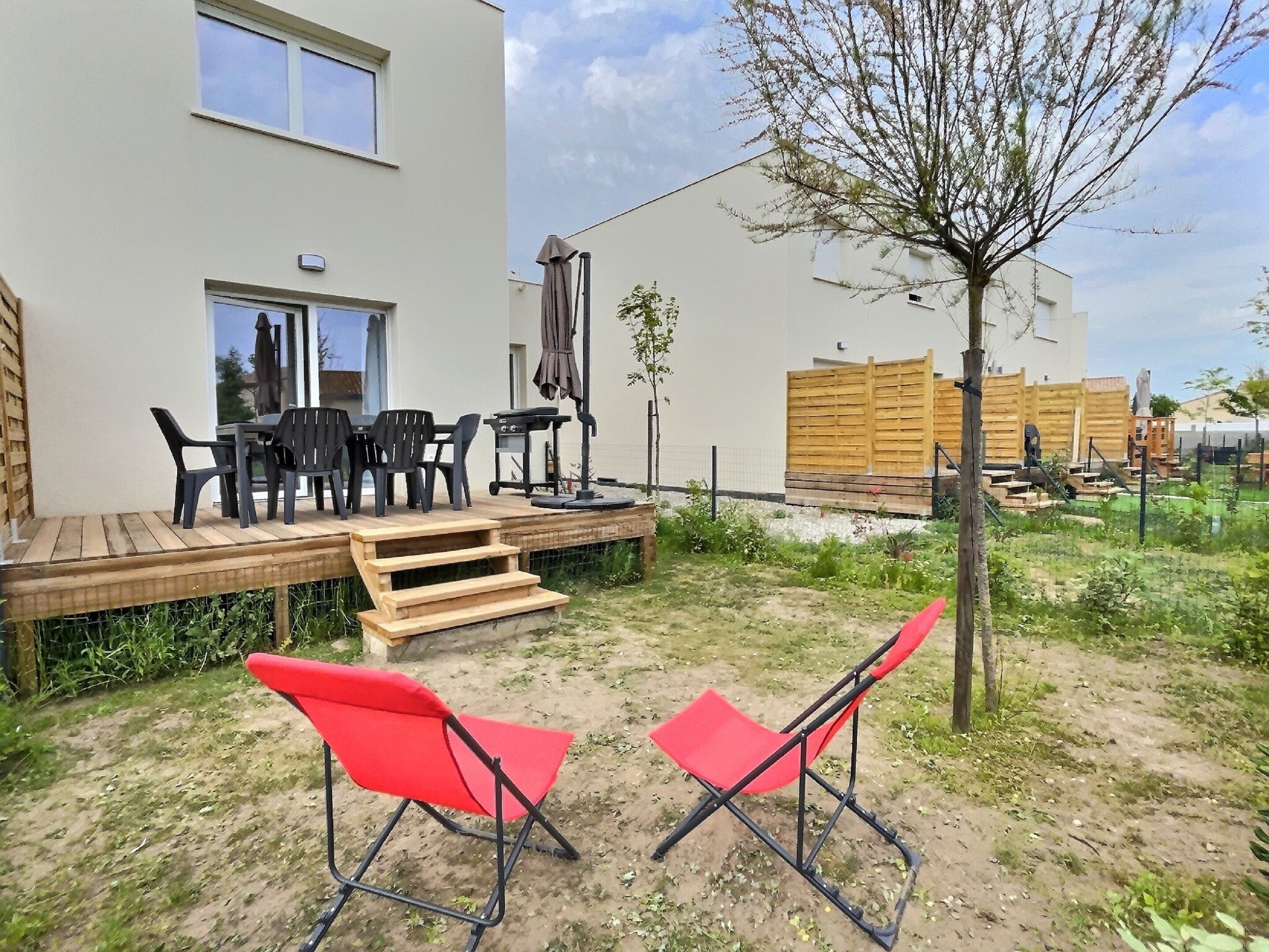 Um pátio com móveis de exterior, um deck de madeira e uma área de jardim murada.