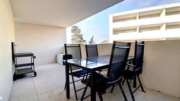 A balcony with a glass table and four chairs, a small shelf, and a cart.