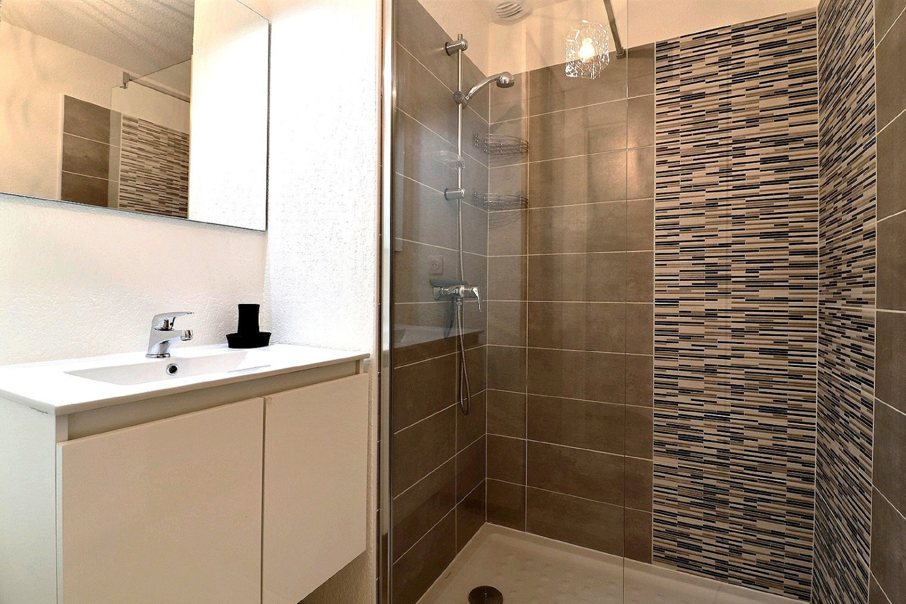 A modern bathroom with a glass-enclosed shower, a white sink, and a mirror.