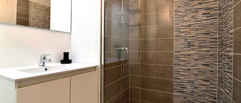Ein modernes Badezimmer mit einer begehbaren Glasdusche, einem weißen Waschbecken und einem Spiegel.