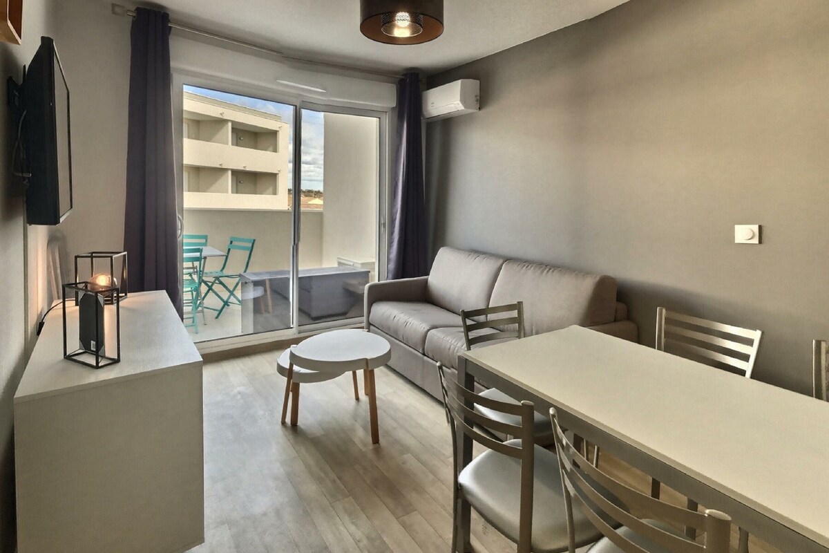 Un salon moderne avec un canapé, une table à manger et un balcon offrant une vue sur les immeubles.