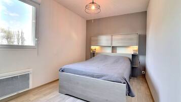 A bedroom with a bed, a window, a radiator, and a ceiling light.