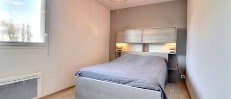 A bedroom with a bed, a window, a radiator, and a ceiling light.