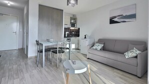 Una sala de estar moderna con un sofá gris, una mesa de comedor con sillas y una cocina al fondo.