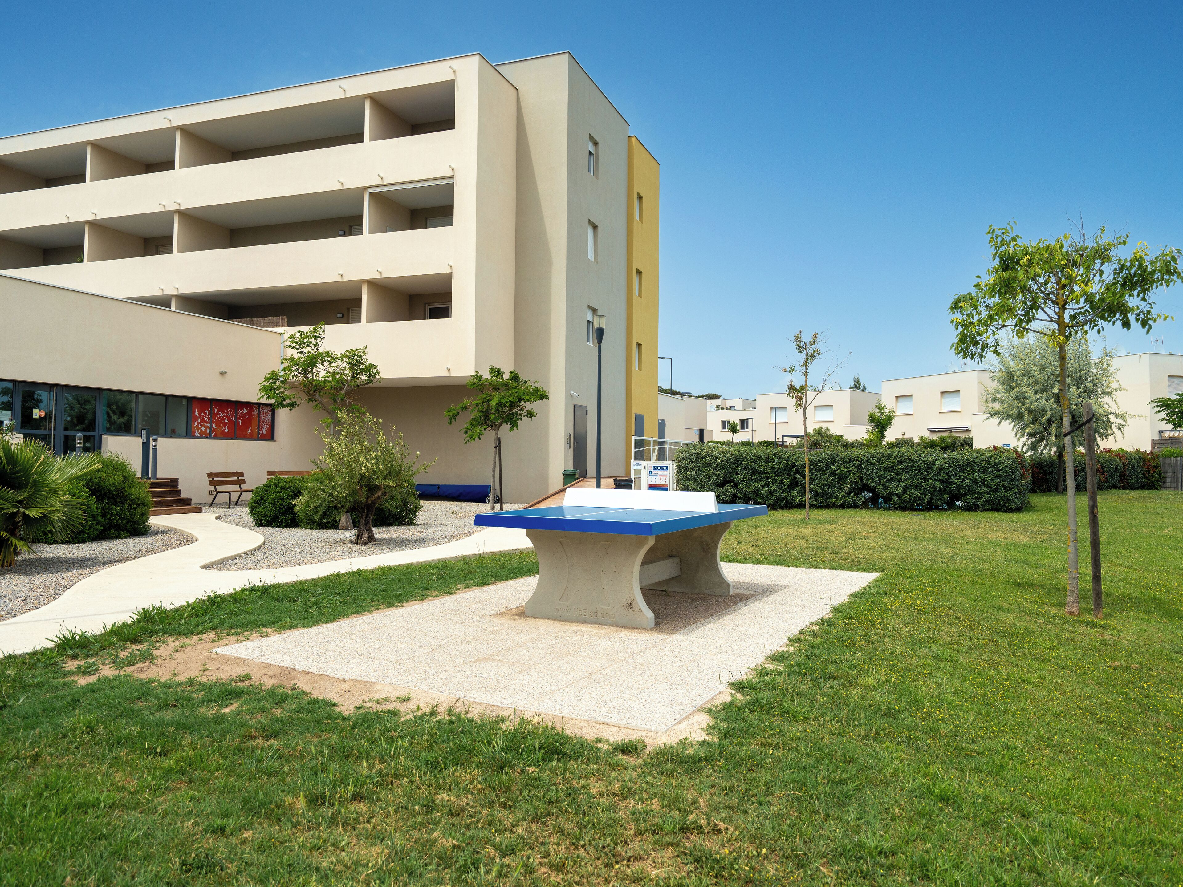 A modern building with multiple floors and a courtyard featuring a concrete table, benches, and greenery.