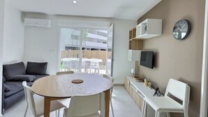 Una sala de estar moderna con una mesa redonda de madera, sillas blancas, un sofá gris y un televisor montado en la pared.