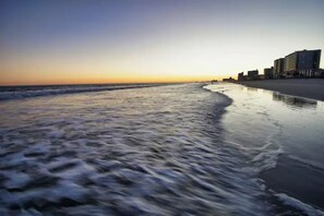 Ein Strand mit ruhiger See, feuchtem Sandstrand und Gebäuden im Hintergrund.