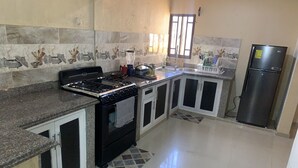 A kitchen with a stove, oven, refrigerator, and a window with bars.