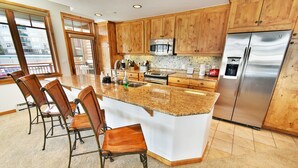 A kitchen with wooden cabinets, a stainless steel refrigerator, a granite countertop, and a dining area with chairs. - Lake View! 3 Kings. Elevator, Hot Tubs. On Lake Rec Path. Walk to Dining (Frisco)