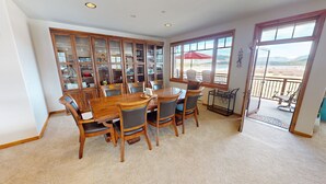A dining area with a wooden table and chairs, a glass cabinet with kitchenware, and a view of the outdoors through large windows. - Lake View! 3 Kings. Elevator, Hot Tubs. On Lake Rec Path. Walk to Dining (Frisco)