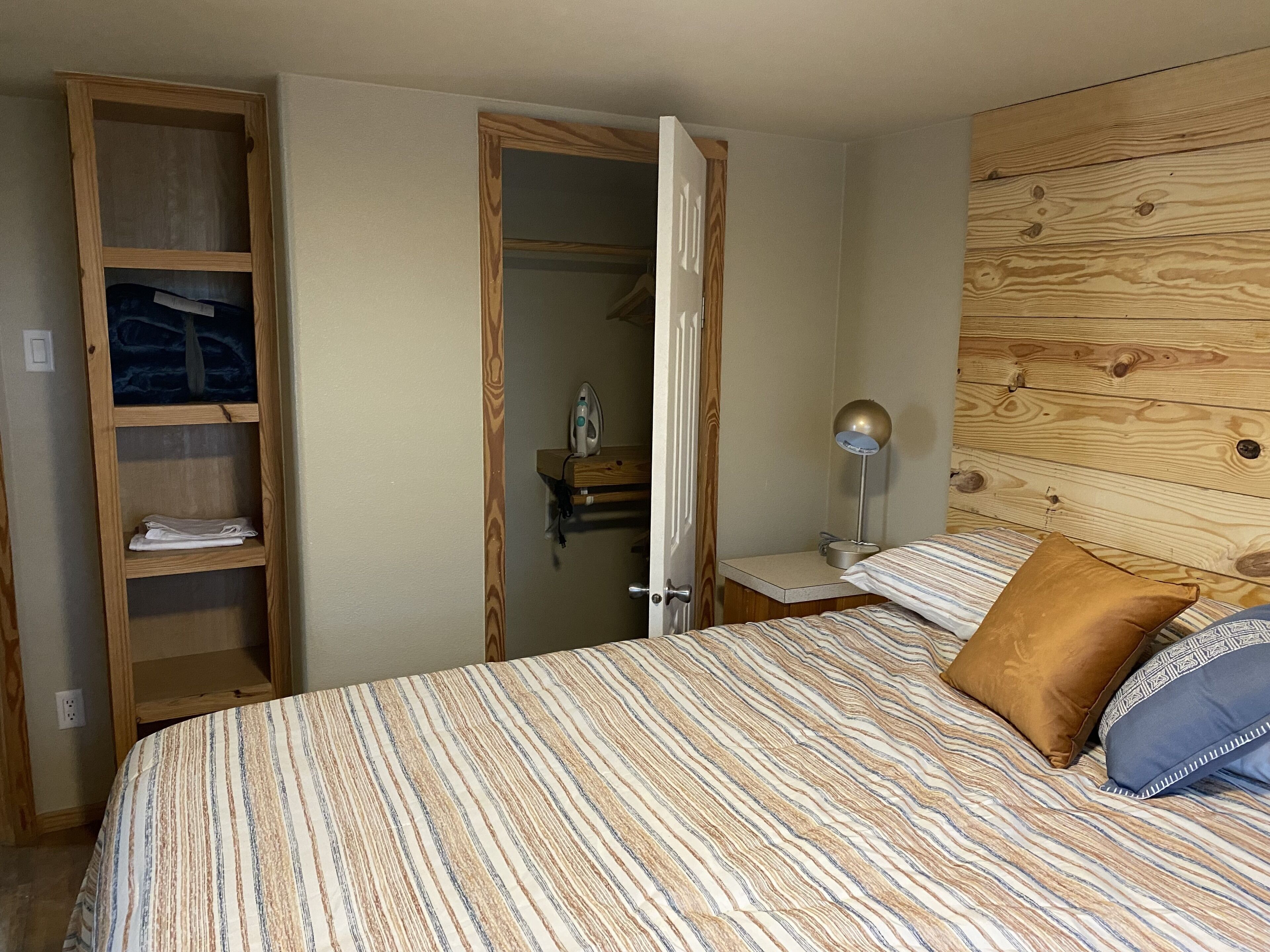 Een slaapkamer met een bed, een houten hoofdbord, een nachtkastje, een lamp en een kledingkast.